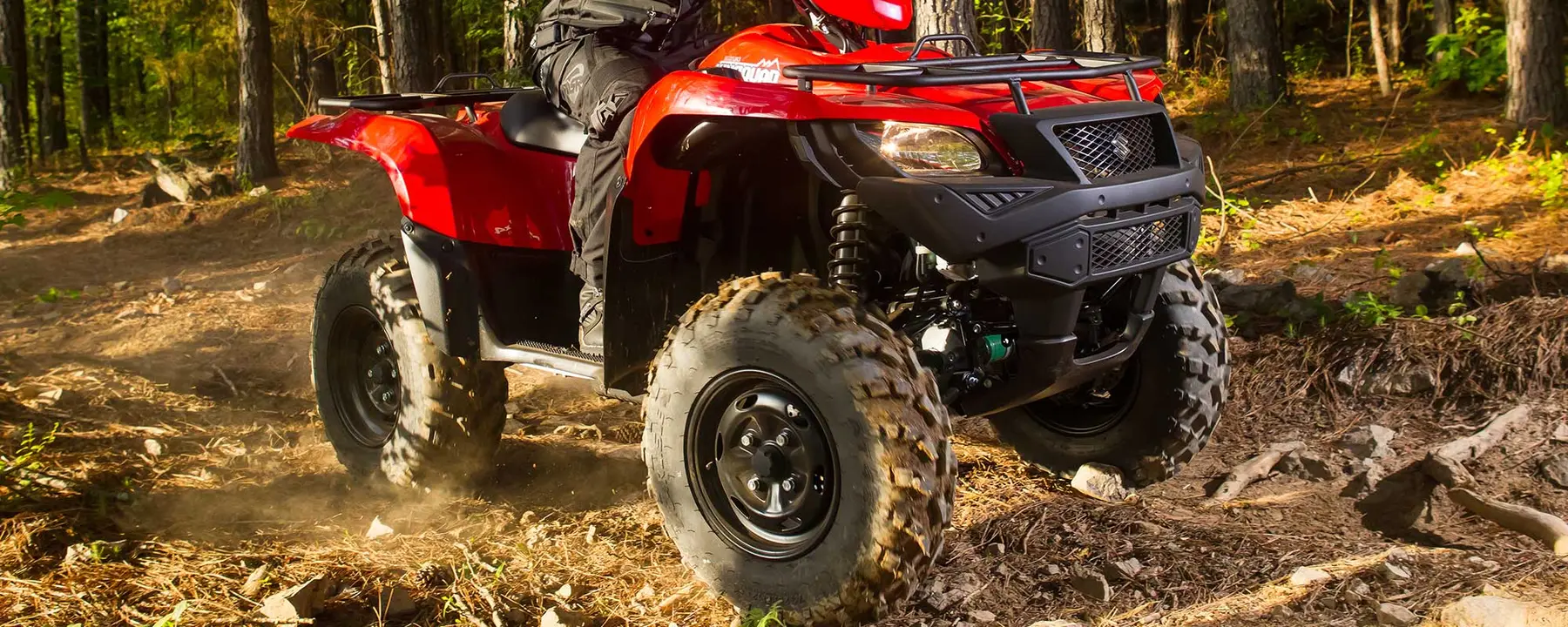 Red Suzuki KingQuad riding on a gravel trail